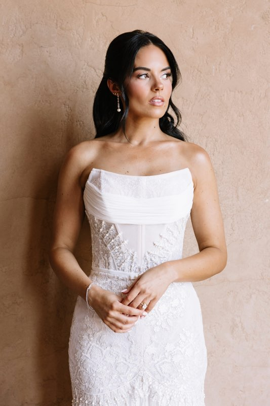 Bride in a white lace gown against a warm textured wall